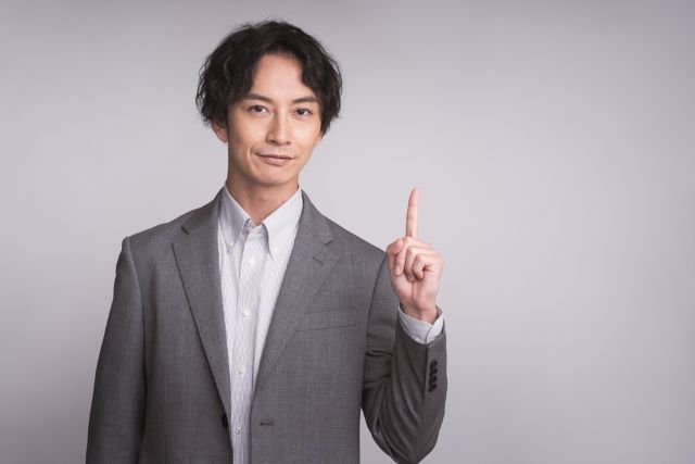 人差し指を立てるスーツの男性